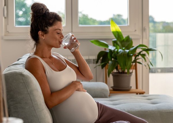 Zwangere vouw drie drinkt in een waterglas